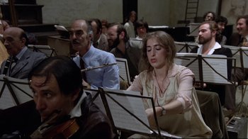 Movie still from “Orchestra Rehearsal” (1978), directed by Federico Fellini – A group of people sitting in a room with musical instruments; Medium shot, Over the shoulder angle