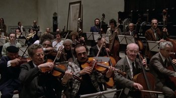 Movie still from “Orchestra Rehearsal” (1978), directed by Federico Fellini – A large group of people playing musical instruments in a room; Wide shot, High angle
