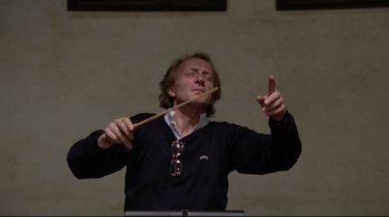 Movie still from “Orchestra Rehearsal” (1978), directed by Federico Fellini – A man is playing a musical instrument while holding a stick; Close Up shot, Low angle