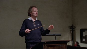Movie still from “Orchestra Rehearsal” (1978), directed by Federico Fellini – A man in a blue sweater is playing a musical instrument; Medium shot, Low angle