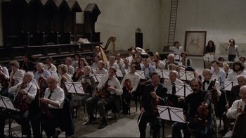 Movie still from “Orchestra Rehearsal” (1978), directed by Federico Fellini – A large group of people sitting in a room with musical instruments; Wide shot, High angle