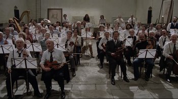 Movie still from “Orchestra Rehearsal” (1978), directed by Federico Fellini – A group of people sitting in chairs holding instruments; Wide shot, High angle