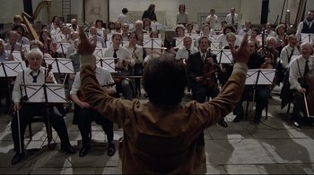 Movie still from “Orchestra Rehearsal” (1978), directed by Federico Fellini – A group of people sitting in a room with their hands raised; Wide shot, High angle