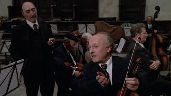 Movie still from “Orchestra Rehearsal” (1978), directed by Federico Fellini – An older man in a suit and tie holding a violin; Medium shot, Low angle