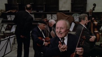 Movie still from “Orchestra Rehearsal” (1978), directed by Federico Fellini – An older man in a suit and tie clapping; Medium shot, Low angle