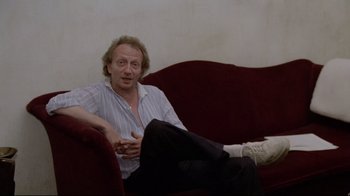Movie still from “Orchestra Rehearsal” (1978), directed by Federico Fellini – A man sitting on top of a red couch; Medium shot, Low angle