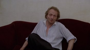 Movie still from “Orchestra Rehearsal” (1978), directed by Federico Fellini – A man sitting on top of a red couch in a room; Medium shot, High angle