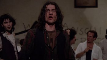 Movie still from “Orchestra Rehearsal” (1978), directed by Federico Fellini – A man with long black hair standing in front of a wall; Medium shot, Low angle