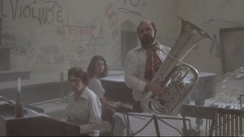 Movie still from “Orchestra Rehearsal” (1978), directed by Federico Fellini – A man and a woman are playing the tuba while a woman watches; Wide shot, Low angle