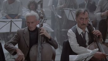 Movie still from “Orchestra Rehearsal” (1978), directed by Federico Fellini – A man playing a contrabass in front of a group of people; Medium shot, Low angle