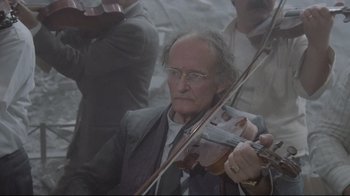 Movie still from “Orchestra Rehearsal” (1978), directed by Federico Fellini – An older man playing a violin in front of a group of people; Close Up shot, Low angle