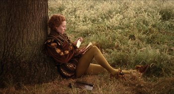 Movie still from “Orlando” (1992), directed by Sally Potter – A woman sitting on the ground reading a book next to a tree; Wide shot, High angle