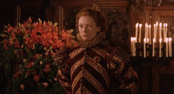 Movie still from “Orlando” (1992), directed by Sally Potter – A woman dressed in renaissance clothing standing in front of a flower arrangement; Medium shot, Low angle