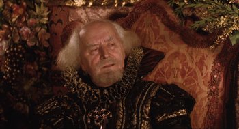 Movie still from “Orlando” (1992), directed by Sally Potter – An old man with a white beard wearing a black and gold outfit; Close Up shot, Over the shoulder angle