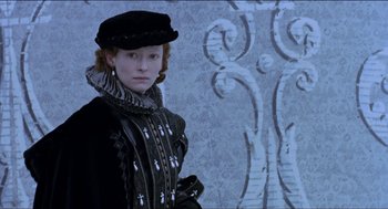 Movie still from “Orlando” (1992), directed by Sally Potter – A woman dressed in renaissance garb standing in front of a wall; Medium shot, Low angle
