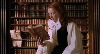 Movie still from “Orlando” (1992), directed by Sally Potter – A woman sitting in front of a book in a room full of bookshelves; Medium shot, High angle