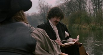Movie still from “Orlando” (1992), directed by Sally Potter – A man writing on a piece of paper while standing next to another man; Medium shot, Over the shoulder angle