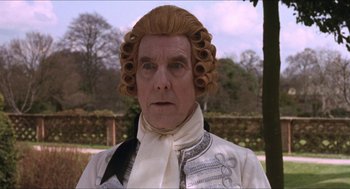 Movie still from “Orlando” (1992), directed by Sally Potter – A man in a wig wearing a white shirt and a black bow tie; Close Up shot, Over the shoulder angle