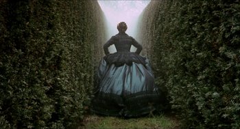 Movie still from “Orlando” (1992), directed by Sally Potter – A woman in a long black and blue dress standing between two bushes; Wide shot, Overhead angle