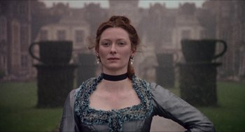 Movie still from “Orlando” (1992), directed by Sally Potter – A woman in a gray and black dress standing in front of a building; Close Up shot, Low angle