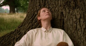 Movie still from “Orlando” (1992), directed by Sally Potter – A woman leaning up against a tree looking up; Close Up shot, Low angle