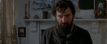 Movie still from “Oscar and Lucinda” (1997), directed by Gillian Armstrong – A man with a beard wearing a vest and standing in front of a fireplace; Close Up shot, Low angle