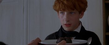 Movie still from “Oscar and Lucinda” (1997), directed by Gillian Armstrong – A young man holding a plate with a brownie on it; Close Up shot, Over the shoulder angle