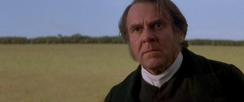 Movie still from “Oscar and Lucinda” (1997), directed by Gillian Armstrong – A man in a black shirt and a white shirt is in a field; Close Up shot, Over the shoulder angle