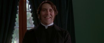 Movie still from “Oscar and Lucinda” (1997), directed by Gillian Armstrong – A man in a priest's outfit smiling for the camera; Close Up shot, Low angle