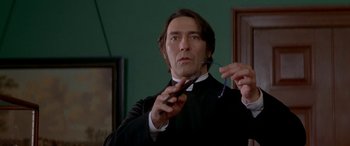 Movie still from “Oscar and Lucinda” (1997), directed by Gillian Armstrong – A man in a black robe holding a pair of scissors in his hand; Close Up shot, Low angle