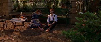 Movie still from “Oscar and Lucinda” (1997), directed by Gillian Armstrong – A man and a woman sitting on the ground next to a bench; Wide shot, High angle