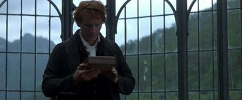 Movie still from “Oscar and Lucinda” (1997), directed by Gillian Armstrong – A man is looking at a book in front of a window; Medium shot, Low angle