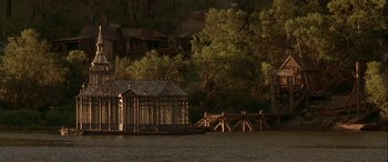 Movie still from “Oscar and Lucinda” (1997), directed by Gillian Armstrong – A wooden structure sitting on top of a body of water near trees; Extreme Wide shot, High angle
