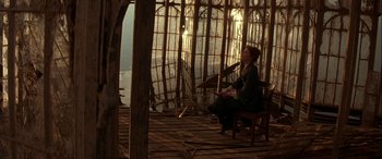 Movie still from “Oscar and Lucinda” (1997), directed by Gillian Armstrong – A woman sitting on a chair in front of a wooden structure; Wide shot, High angle