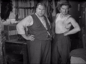 Movie still from “Obsession” (1943), directed by Luchino Visconti – A couple of men standing next to each other in a room; Medium shot, Low angle
