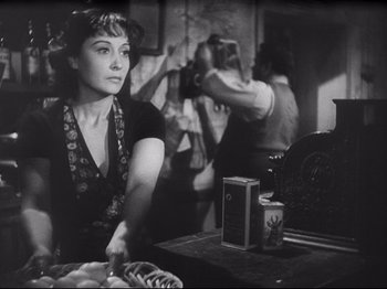 Movie still from “Obsession” (1943), directed by Luchino Visconti – A black - and - white photo of a woman cutting food; Medium shot, Over the shoulder angle