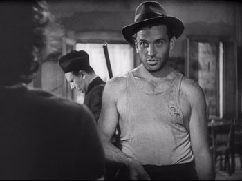 Movie still from “Obsession” (1943), directed by Luchino Visconti – A black and white photo of a man in a hat; Medium shot, Over the shoulder angle