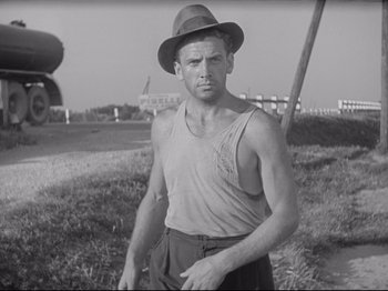 Movie still from “Obsession” (1943), directed by Luchino Visconti – A man wearing a hat standing in the grass; Medium shot, Low angle