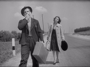 Movie still from “Obsession” (1943), directed by Luchino Visconti – A man and a woman walking down a road with suitcases; Medium shot, Low angle