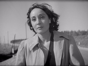 Movie still from “Obsession” (1943), directed by Luchino Visconti – Black and white photograph of a woman wearing a trench coat; Close Up shot, Low angle