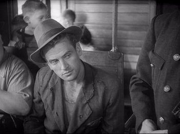 Movie still from “Obsession” (1943), directed by Luchino Visconti – A black and white photo of a man with a hat; Medium shot, Over the shoulder angle