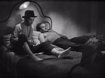 Movie still from “Obsession” (1943), directed by Luchino Visconti – A couple of men sitting on top of a bed next to each other; Medium shot, High angle
