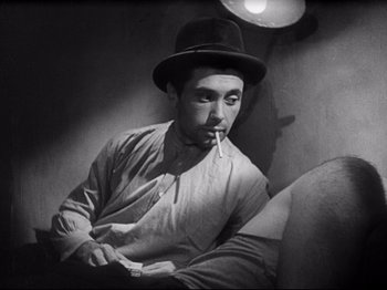 Movie still from “Obsession” (1943), directed by Luchino Visconti – A black and white photo of a man smoking a cigarette; Medium shot, Low angle