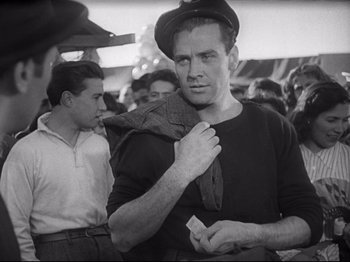 Movie still from “Obsession” (1943), directed by Luchino Visconti – A black and white photo of a man in a crowd; Medium shot, Low angle