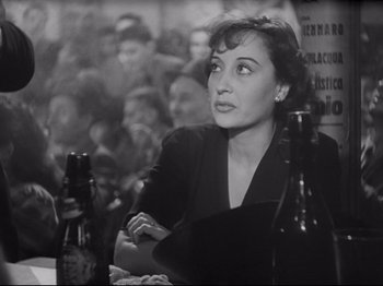Movie still from “Obsession” (1943), directed by Luchino Visconti – A woman sitting at a table in front of a group of people; Close Up shot, High angle