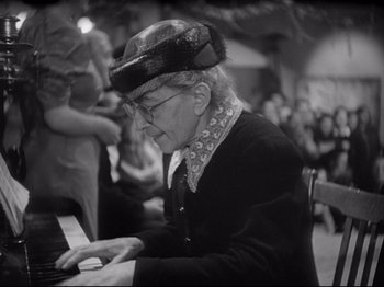 Movie still from “Obsession” (1943), directed by Luchino Visconti – An older man playing the piano at a party; Close Up shot, High angle