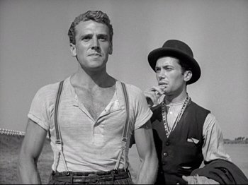 Movie still from “Obsession” (1943), directed by Luchino Visconti – Two men standing next to each other in front of a wall; Medium shot, Low angle