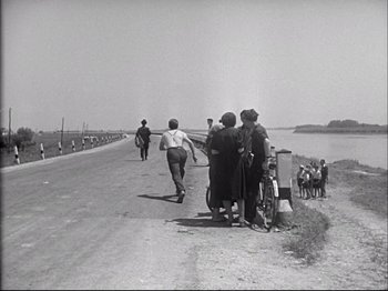 Movie still from “Obsession” (1943), directed by Luchino Visconti – A black and white photo of people walking down a road; Wide shot, High angle