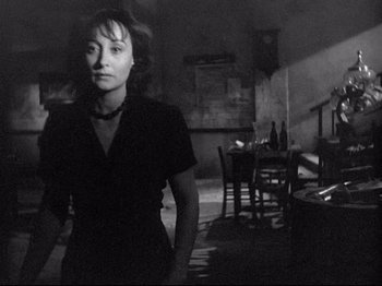 Movie still from “Obsession” (1943), directed by Luchino Visconti – A black and white photo of a woman standing in front of a dining room table; Medium shot, Over the shoulder angle