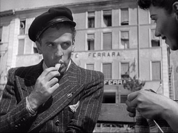 Movie still from “Obsession” (1943), directed by Luchino Visconti – A man wearing a hat and smoking a cigarette; Medium shot, Low angle